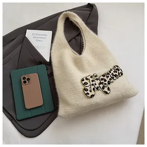 Detalle de bolso tote de punto crema con bordado de leopardo junto a una americana gris