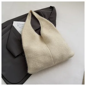 Detalle de bolso de hombro de punto crema sobre chaqueta gris con vista de textura