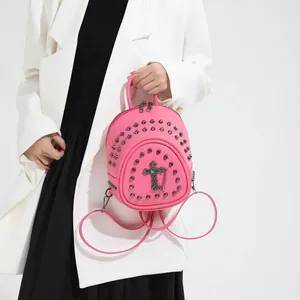 Mini sac à dos rose vif avec rivets et croix porté par un mannequin en blanc