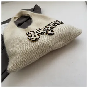 Primer plano del bolso de punto crema con textura afelpada y detalle de letra de leopardo