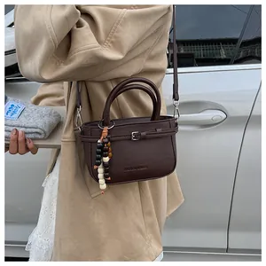 Detail of dark brown leather handbag with metal buckle and tricolor wooden bead charm