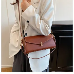 Detail of a brown leather crossbody bag with a minimalist golden metal lock buckle