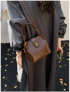 Detail of dark brown bucket bag with gold twist-lock and cherry charm against fall outfit