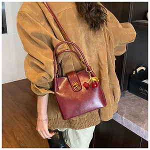 Close-up of wine red bucket bag featuring gold twist lock and cherry charm detail