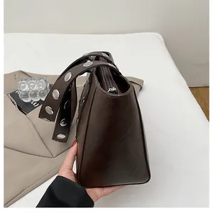 Close-up of retro dark brown tote bag featuring silver studs on the wide shoulder strap
