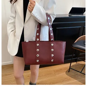 Detail of burgundy leather shoulder bag featuring silver metal rivets on white suit
