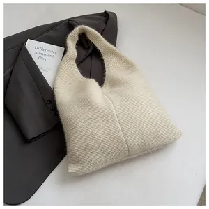 Close-up of off-white knitted tote bag texture with minimalist hobo design on dark blazer