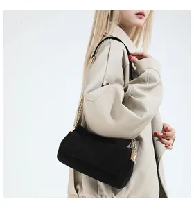 Detail einer schwarzen Wildledertasche mit goldener Kette auf einer beigen Jacke