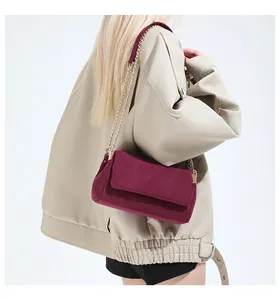 Details einer burgunderroten Wildledertasche mit Goldkette auf einer beigen Lederjacke