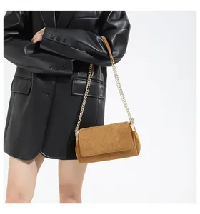 Detailansicht der braunen Wildledertasche mit goldener Kette auf einem schwarzen Lederblazer