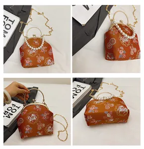 Detail of orange satin shell bag with floral embroidery and pearl handle strap