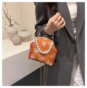 Detail of orange brocade shell bag with floral patterns and pearl bead handle