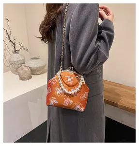 Close-up of orange silk shell bag with dragon embroidery and pearl handle strap