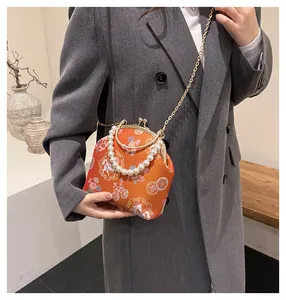 Detail of a bright orange shell bag with pearl handle and traditional floral patterns