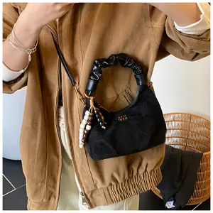 Close-up of black crescent suede handbag featuring diamond quilting and beaded tassel