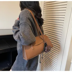 Brown leather tote bag with pebble texture and mini pouch pendant on a gray sweater