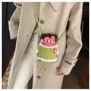 Detail of a handmade green crochet monster crossbody bag with pink flower and bow accents