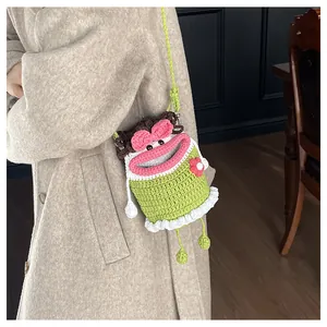 Detail view of handmade knit green crossbody bag with cartoon face and floral accents
