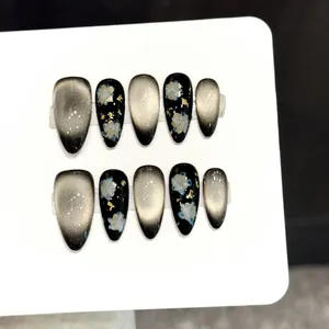 Handmade black and gold cat eye press-on nails with floral patterns and gold foil flakes