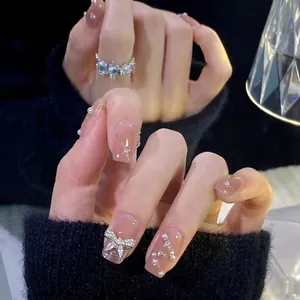 Détails des faux ongles faits main pêche avec nœud argenté et décorations en cristal