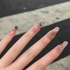 Detail of long ballerina nails with nude gradient, blue teardrop diamond and rhinestones