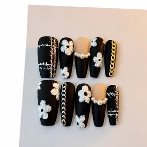 Handmade black press-on nails featuring 3D floral designs and pearl chain accents