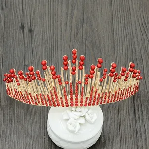 Elegant gold bridal crown with red pearls and rhinestones on a white ceramic stand