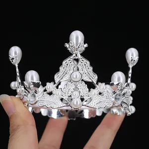 Silver baroque tiara with pearls and rhinestones held by hand against black background