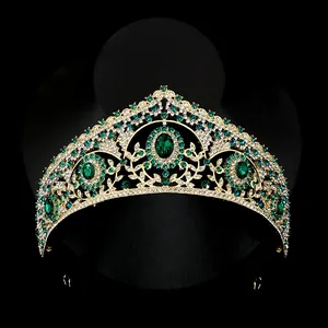 Baroque gold crown with emerald green gems and white crystals on black background