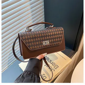Vue détaillée du sac bandoulière marron à damier avec boucle argentée tenu dans un cadre chic