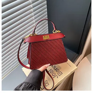Detail of dark red handbag with woven texture and gold twist-lock closure on front flap