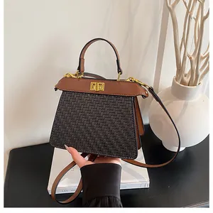 Close-up of black woven trapezoid bag with brown leather flap and gold metal turn-lock