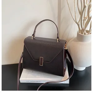 Detail view of dark brown pebbled leather handbag with gold clasp on white books