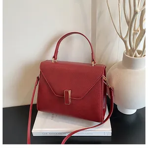 Detail of red litchi texture tote bag with golden metal clasp and top handle on books