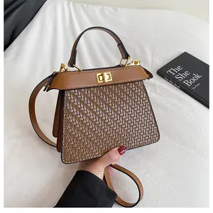 Detail of a brown woven crossbody bag with a golden square twist-lock on white fabric