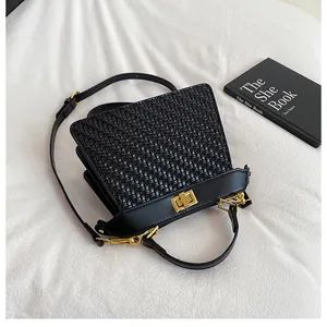 Detail of black woven shoulder bag featuring a gold twist lock and a fine leather strap