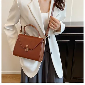 Brown leather tote bag featuring lychee texture and metal buckle on a white blazer model