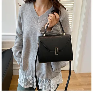 Detail of black pebbled leather tote bag with gold lock worn with a grey knit sweater