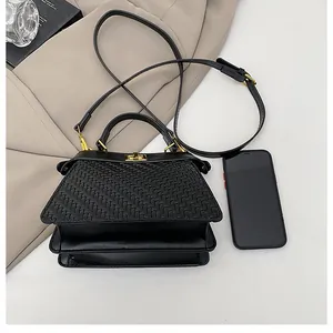Detail of black woven handbag with gold lock beside a phone for size reference