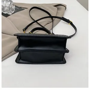 Detail of black crossbody bag featuring woven texture flap and gold metal buckles