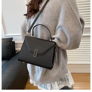 Detail of black pebbled leather tote bag with rectangular metal clasp shown on a model