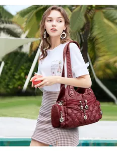 Détail du cuir souple bordeaux avec coutures décoratives et pendentif floral argenté sur le sac