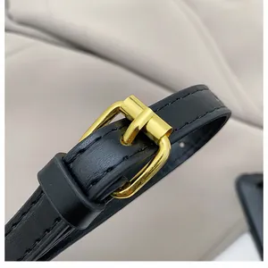 Detail of black faux leather shoulder strap with polished gold-tone metal buckle and stitching