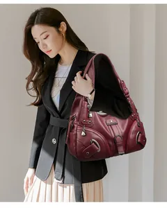 Detailed view of burgundy pebbled leather shoulder bag with silver zippers and metal plate