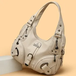Close-up of cream soft leather handbag featuring multi-pocket zippers and metal rivets