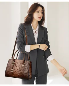 Detailed view of crocodile pattern leather handbag with adjustable strap on a grey suit model