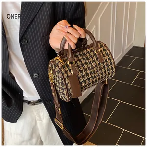 Detail of houndstooth pillow bag featuring brown leather handles and wide fabric strap