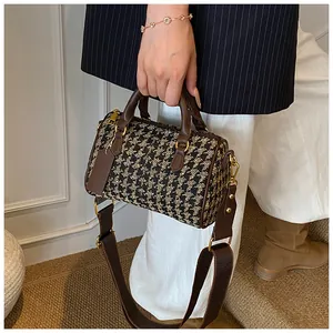 Detail of checkered boston bag with brown leather handles and gold metal hardware