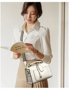 Detail of white snakeskin texture handbag with wide geometric pattern strap and gold hardware