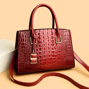 Red crocodile texture handbag with gold hardware and shoulder strap on beige backdrop